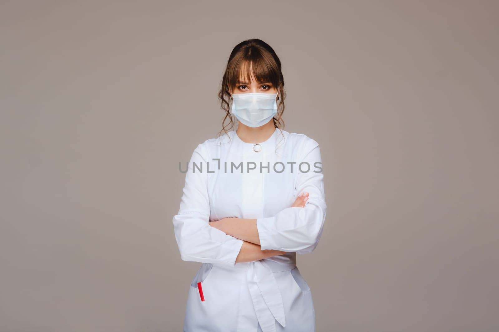 A girl doctor stands in a medical mask, isolated on a gray background. by Lobachad