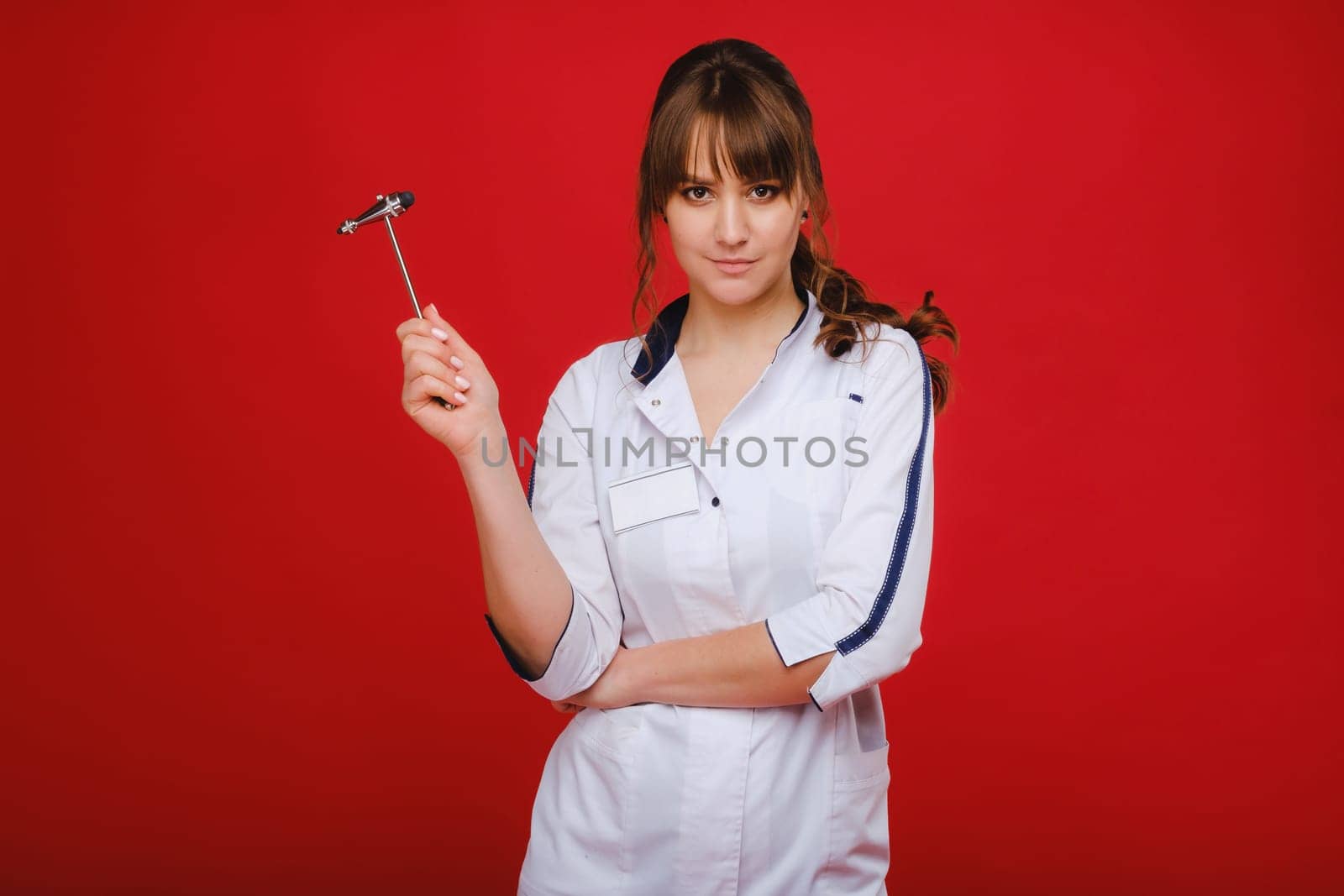 a beautiful doctor girl holds a reflex hammer and smiles at the camera isolated on a Red background by Lobachad