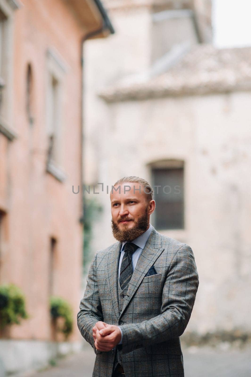 A man with a beard in a strict grey three-piece suit with a tie in the old town of Sirmione, a Stylish man in a grey suit in Italy.