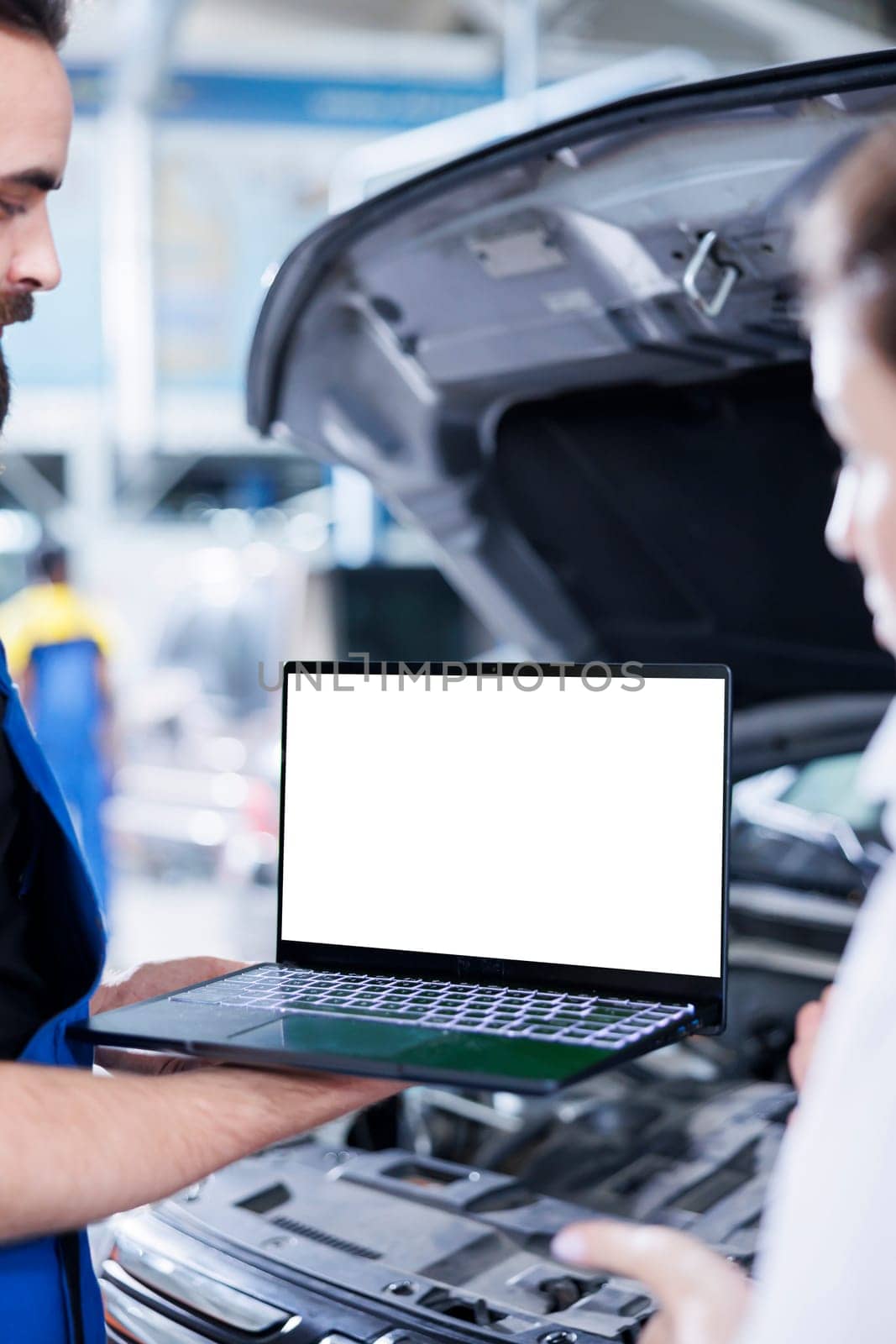 Licensed repairman in garage using mockup laptop to follow checklist while doing maintenance on car. Meticulous expert in auto repair shop does checkup on vehicle helped by isolated screen device