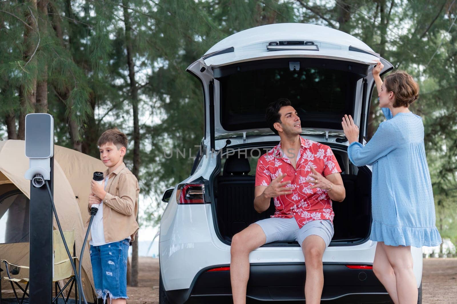 Outdoor adventure and family vacation camping in nature travel by eco friendly car for sustainable future. Lovely family recharge EV car with EV charging station in campsite. Perpetual