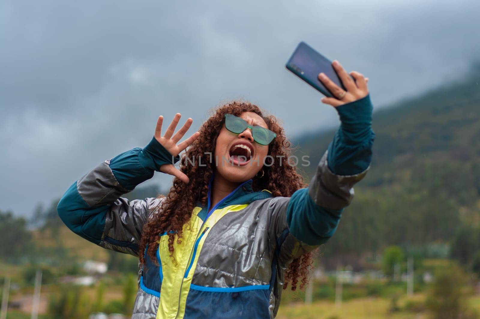 young influencer broadcasting on social networks with an expression of surprise exaggerated in mountain clothes in a mountain. High quality photo
