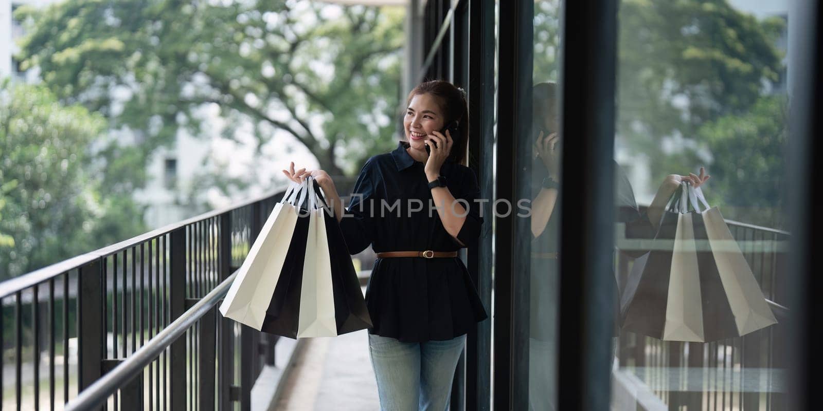 Young woman standing at road holding shopping bags and using mobile phone. Purchases, black friday, discount by itchaznong