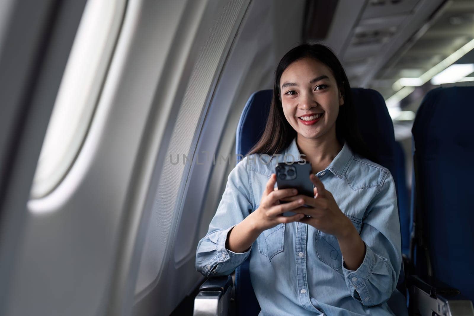 Asian people female person onboard, airplane window, using mobile and looking at camera while on the plane by itchaznong