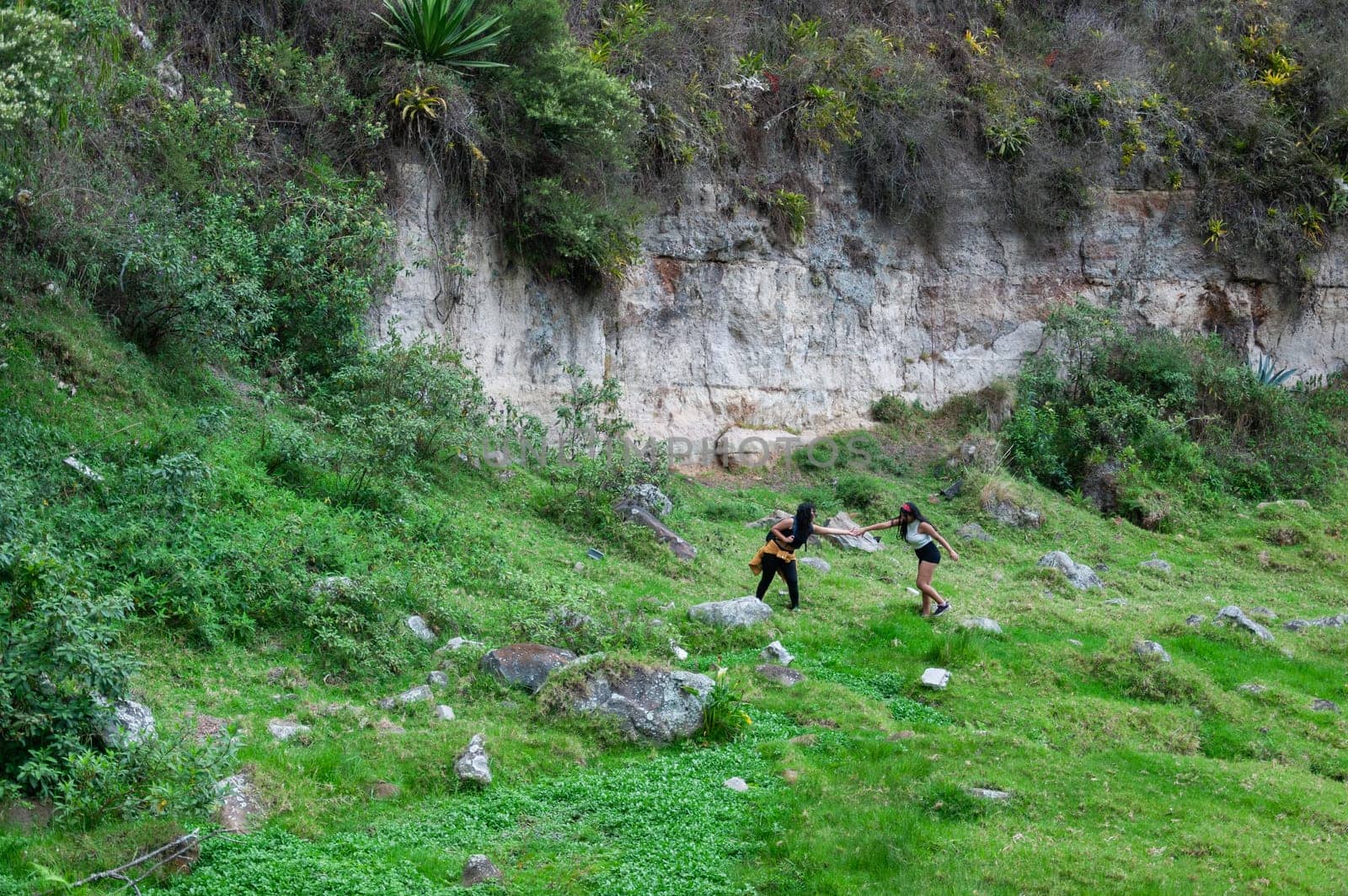 Panoramic view of two friends on a sightseeing tour on their vacation in Ecuador, the girls are helping each other to climb to the top together. by Raulmartin
