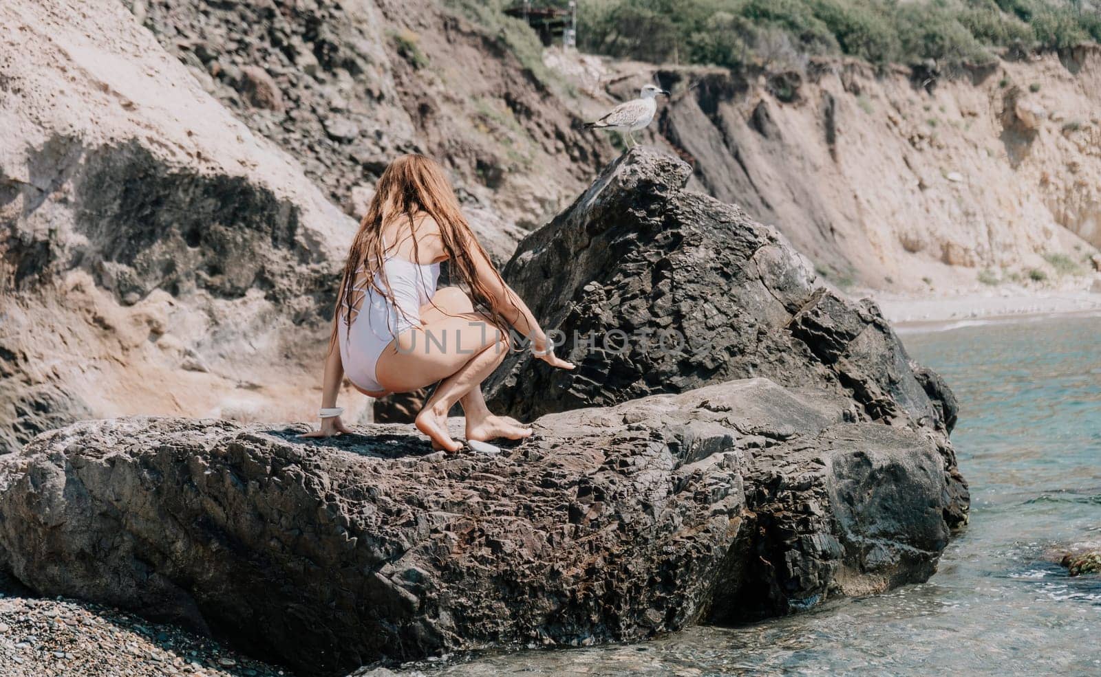 Woman travel sea. Happy tourist in white bikini enjoy taking picture outdoors for memories. Woman traveler posing on the beach at sea surrounded by volcanic mountains, sharing travel adventure journey by panophotograph