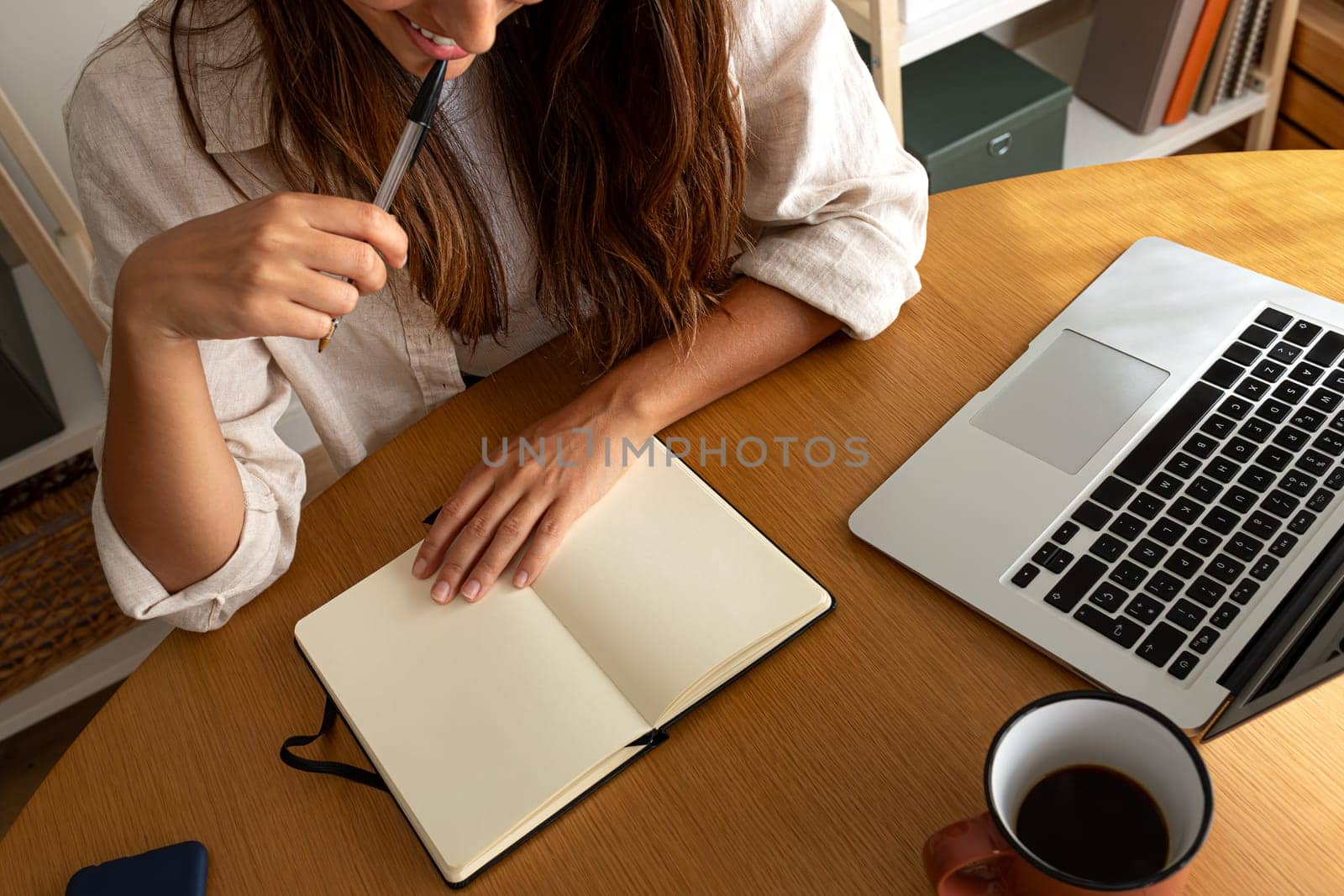 Top view of unrecognisable young woman planning handwriting on notebook while working at home office. Working at home, freelance concept.