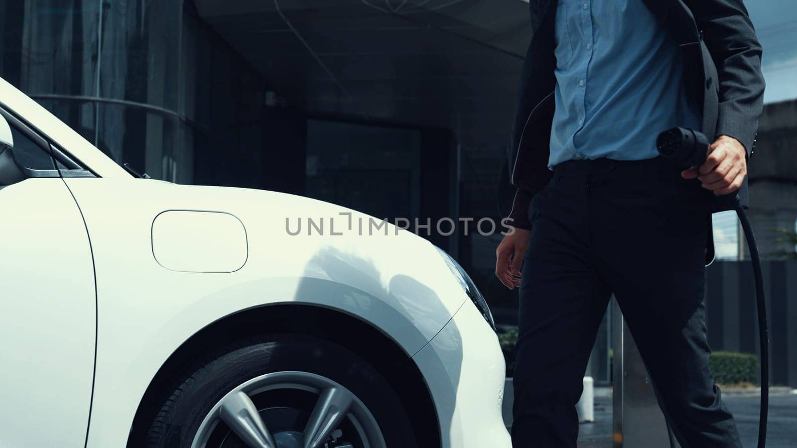 Businessman recharge his electric car from charging station. Peruse by biancoblue