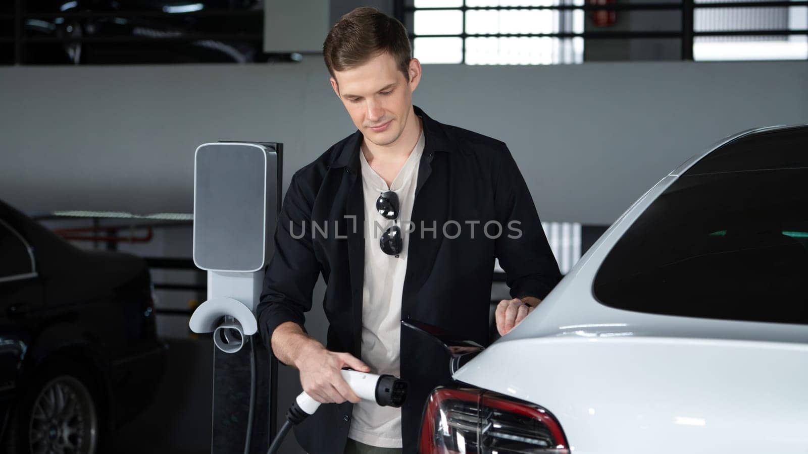 Young man travel with EV electric car to shopping center parking lot innards by biancoblue