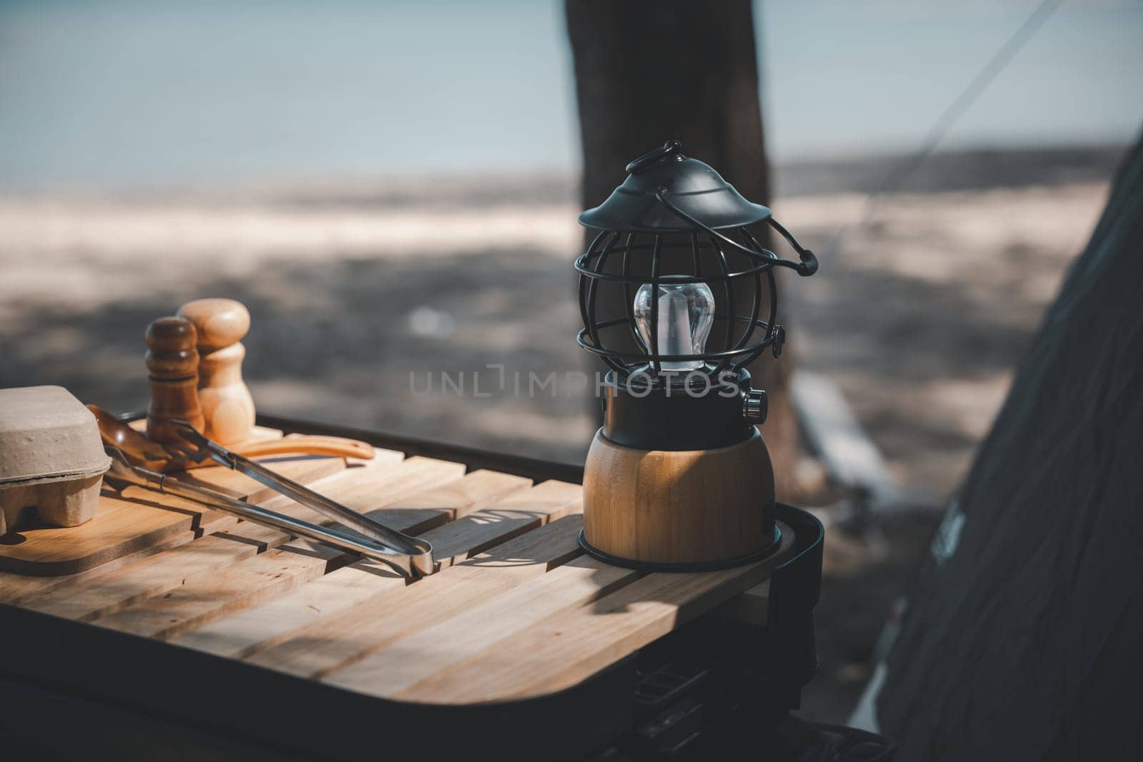 An antique kerosene lantern and a bright LED camping lamp on a wooden table at the beach. Perfect for summer camping and outdoor travel. Old meets new in the great outdoors.