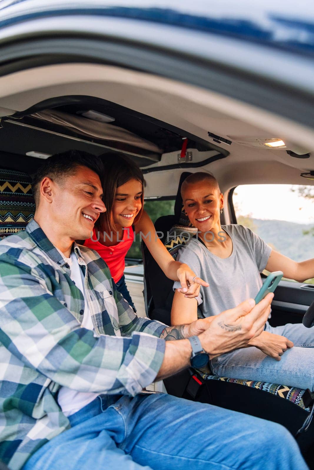 happy family planning on the mobile phone the route through the countryside in their camper van, concept of adventure travel with children and active tourism in nature