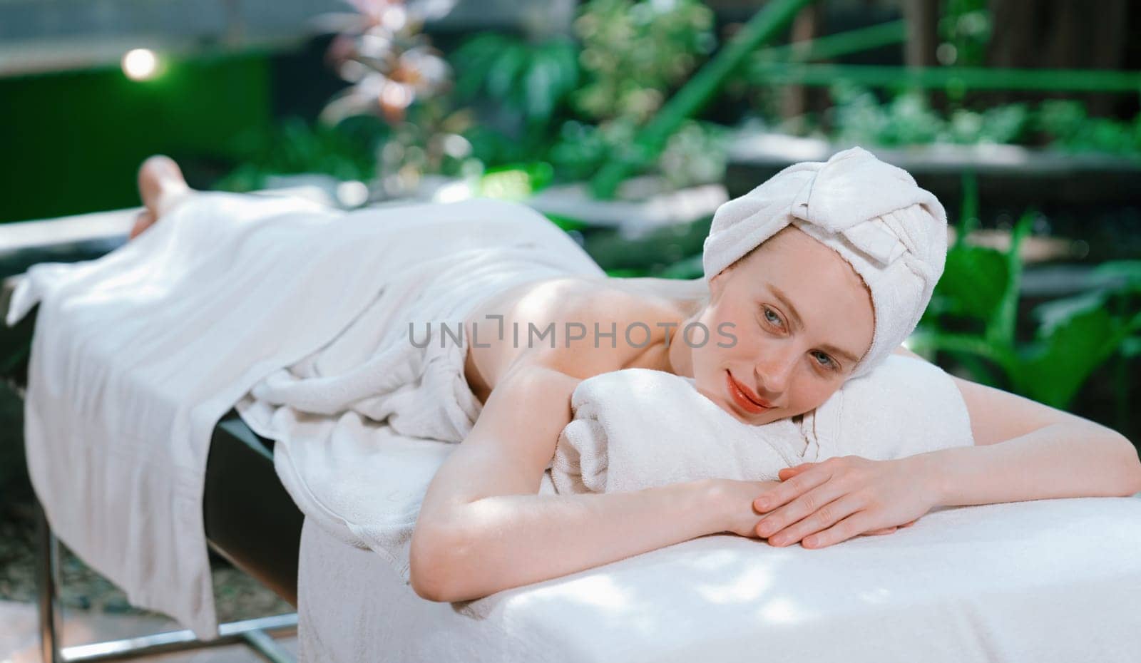 Beautiful young woman relaxes on a spa bed surrounded by nature. ready for a body massage. Attractive female in white towel lying peacefully during waiting for body massage. Close up. Tranquility