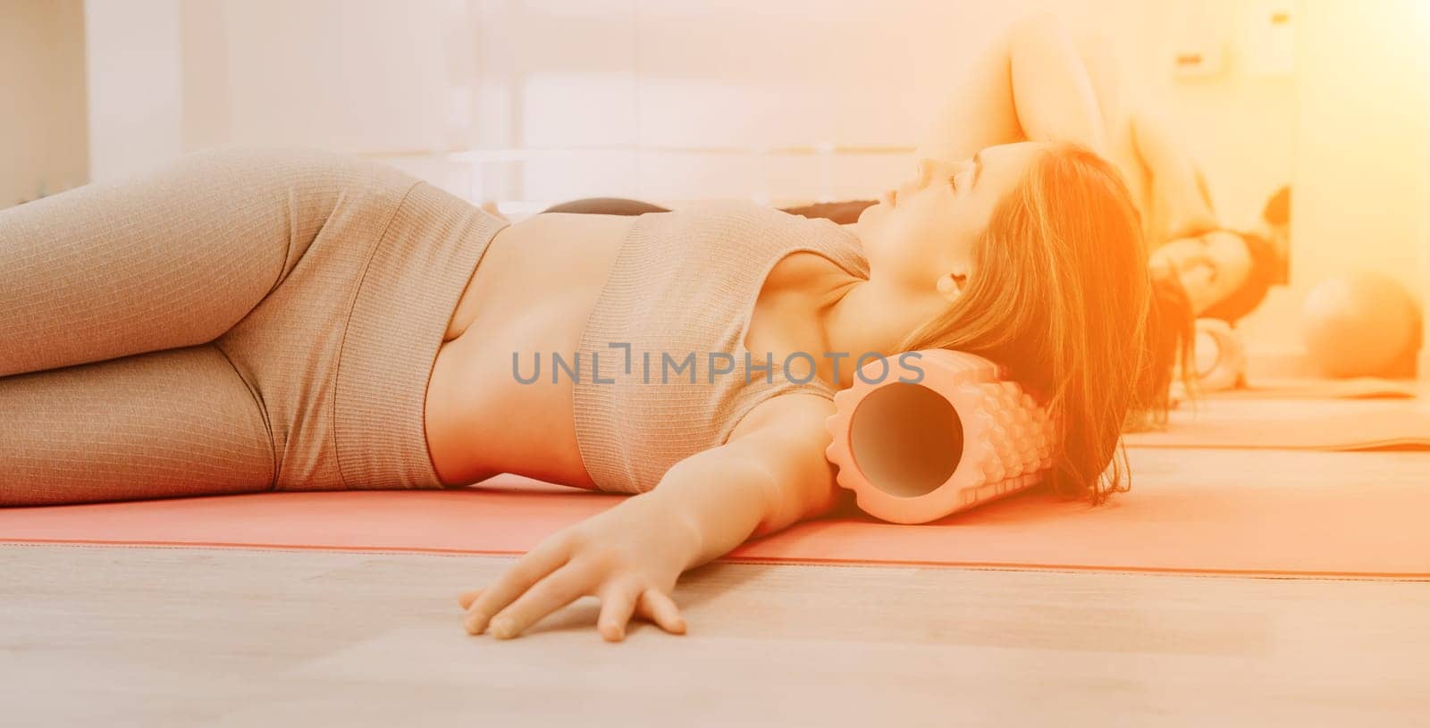 Middle aged well looking women, performing fascia exercises on the floor using a massage foam roller - tool to relieve tension in the back and relieve muscle pain. Female fitness yoga routine concept by panophotograph