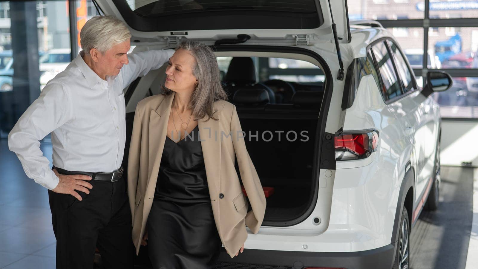 Mature Caucasian couple choosing a car looks at the trunk. by mrwed54