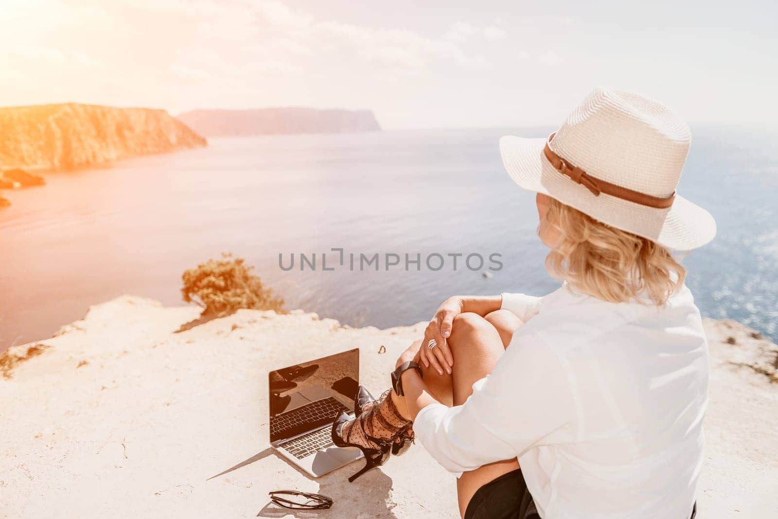 Woman sea laptop. Business woman in yellow hat freelancer with laptop working over blue sea beach. Girl relieves stress from work. Freelance, digital nomad, travel and holidays concept by panophotograph