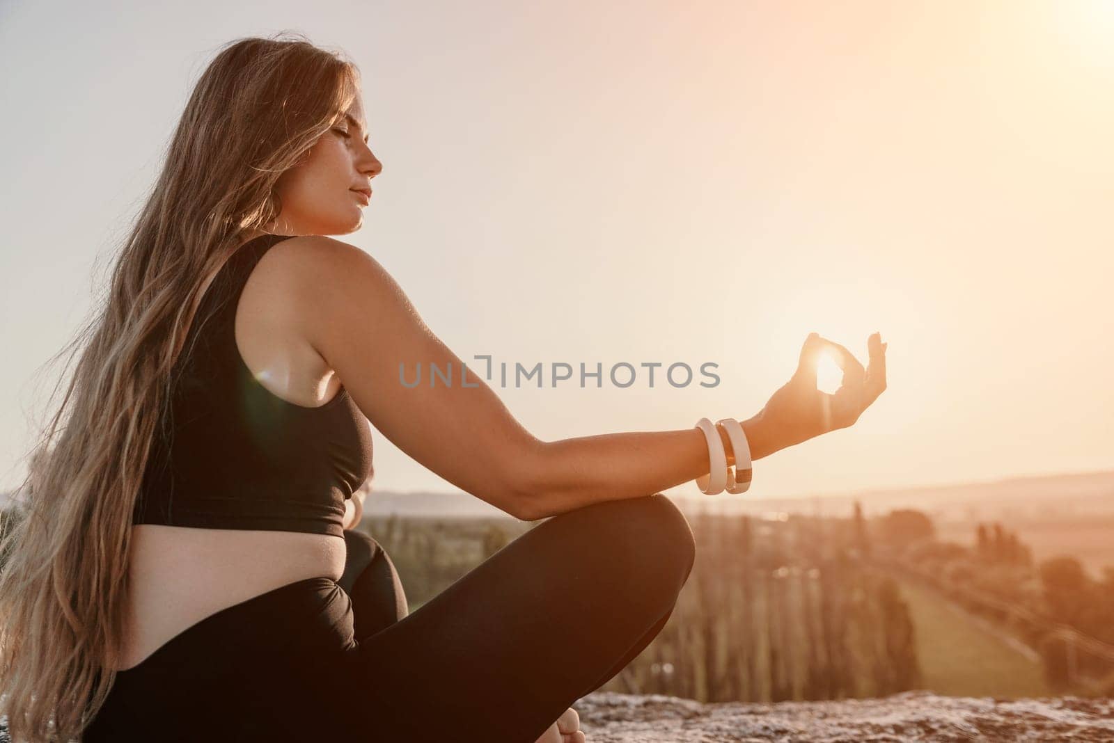 Well looking middle aged woman with long hair, fitness instructor in leggings and tops doing stretching and pilates on the rock near forest. Female fitness yoga routine concept. Healthy lifestyle.