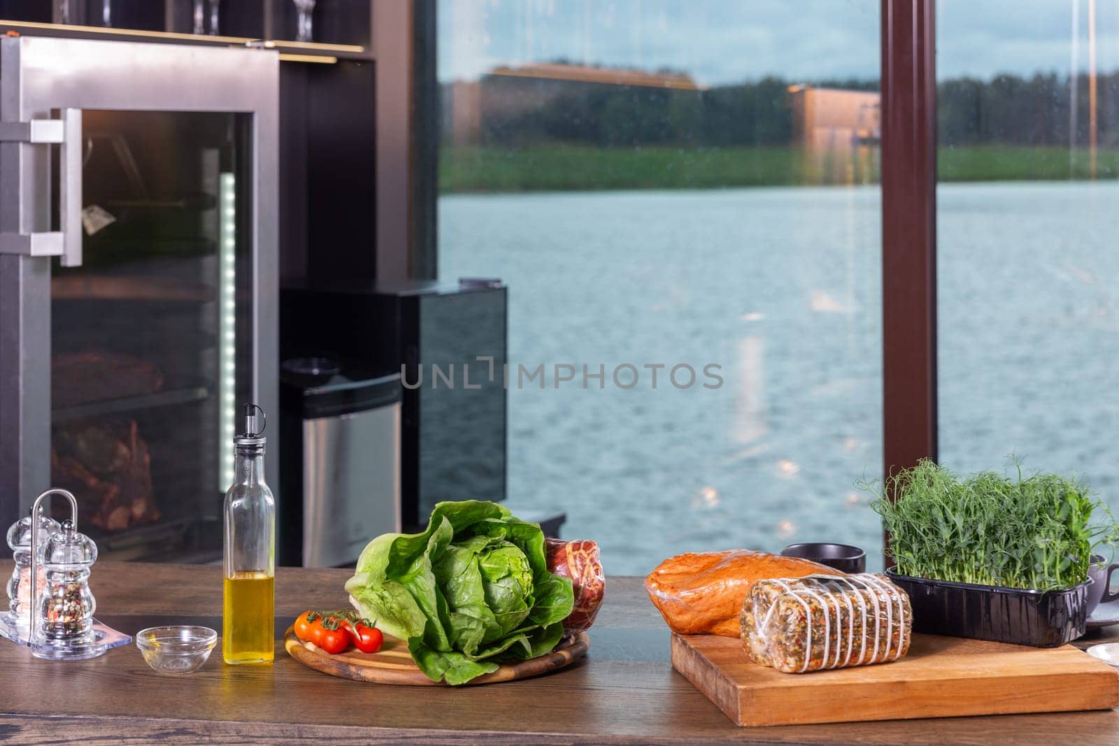 Fresh ingredients for cooking snacks on table. The interior of a modern kitchen with a transparent wall, behind which the surface of the lake is visible.