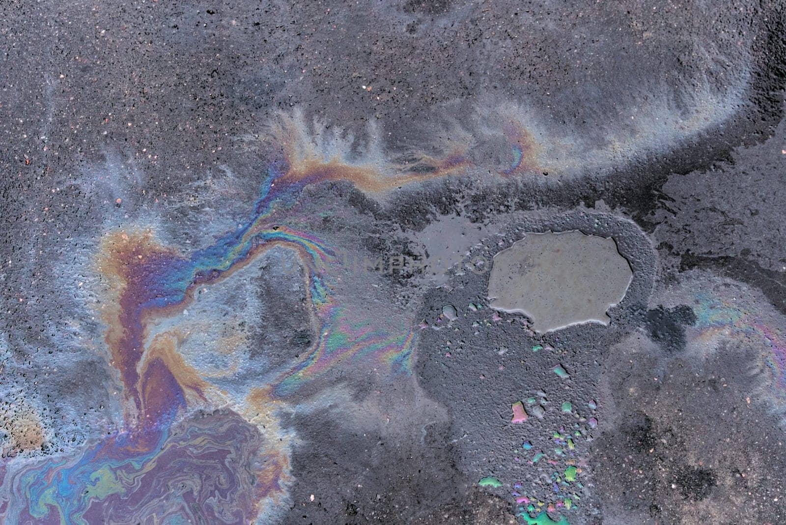 Rainbow-colored oil floating on water after rain on asphalt. Gasoline stains. Colored texture, natural background.