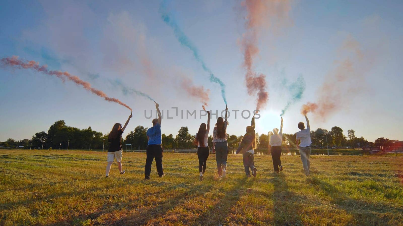 A group of friends spraying multi-colored smoke at sunset. by DovidPro