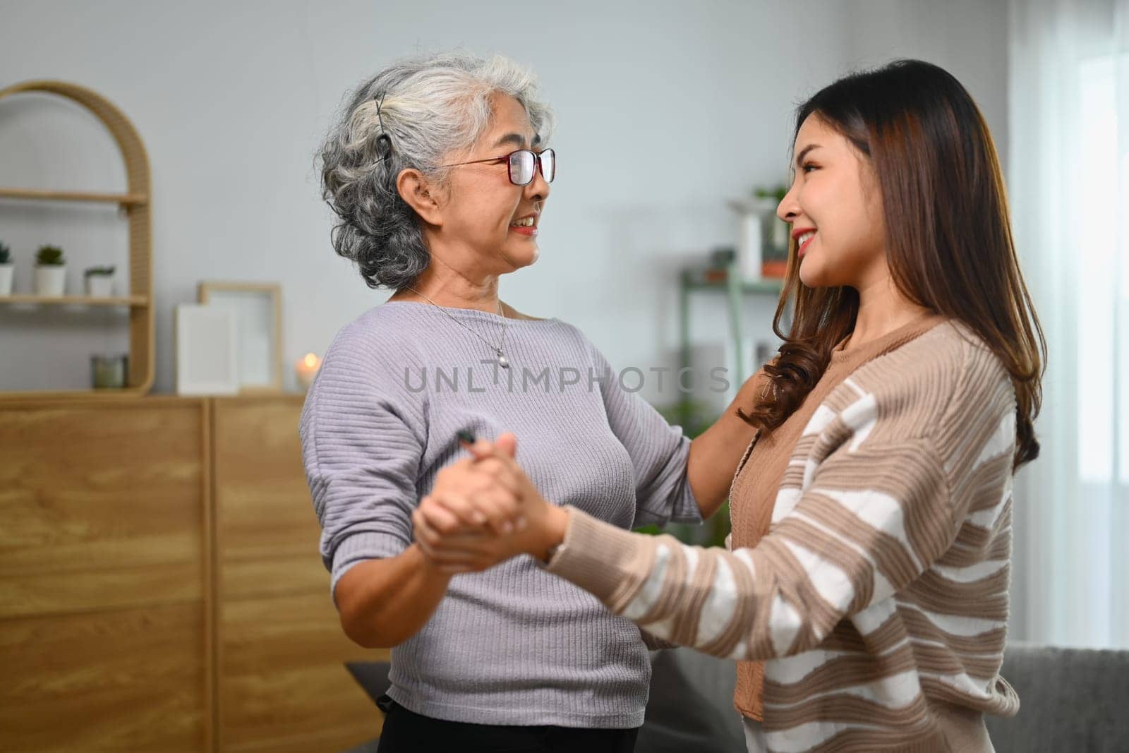 Smiling elderly mother and adult daughter dancing and spending leisure weekend time together at home.