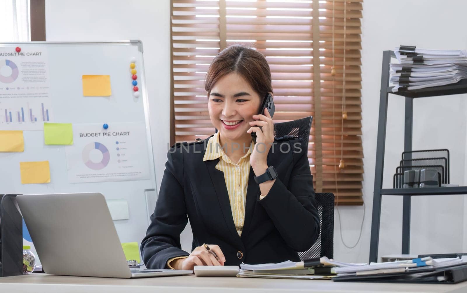 Businesswoman using laptop to do finance, talking on phone, working with numbers on wooden table in office and business background, tax, accounting, statistics and analytical research concept..