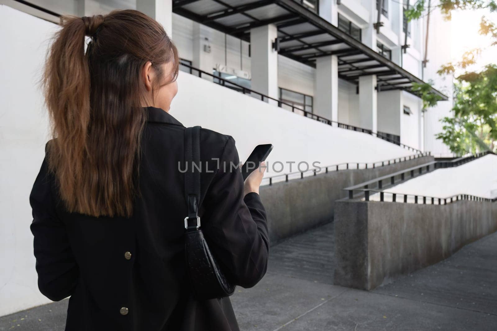 Attractive smiling Asian businesswoman wearing a suit standing in the city using an application on her mobile phone Read news on your smartphone fast connection Check out the outdoor mobile app by wichayada