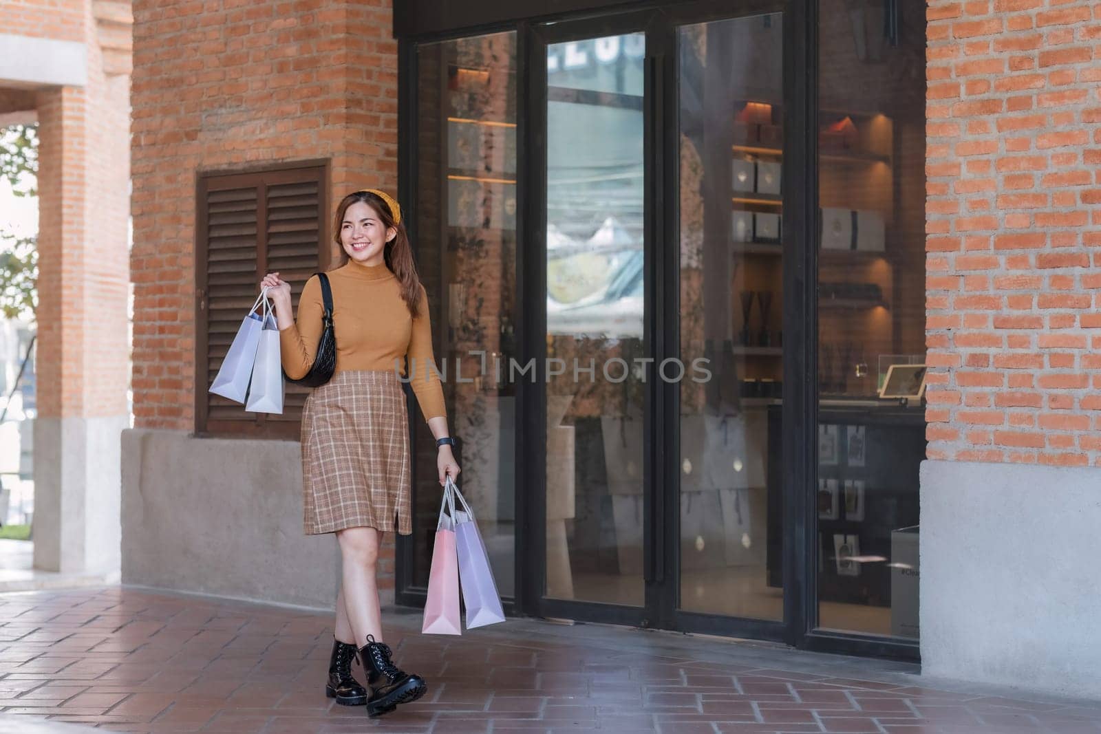 Beautiful Asian woman holding shopping bags and smiling while shopping on Black Friday outside the mall.