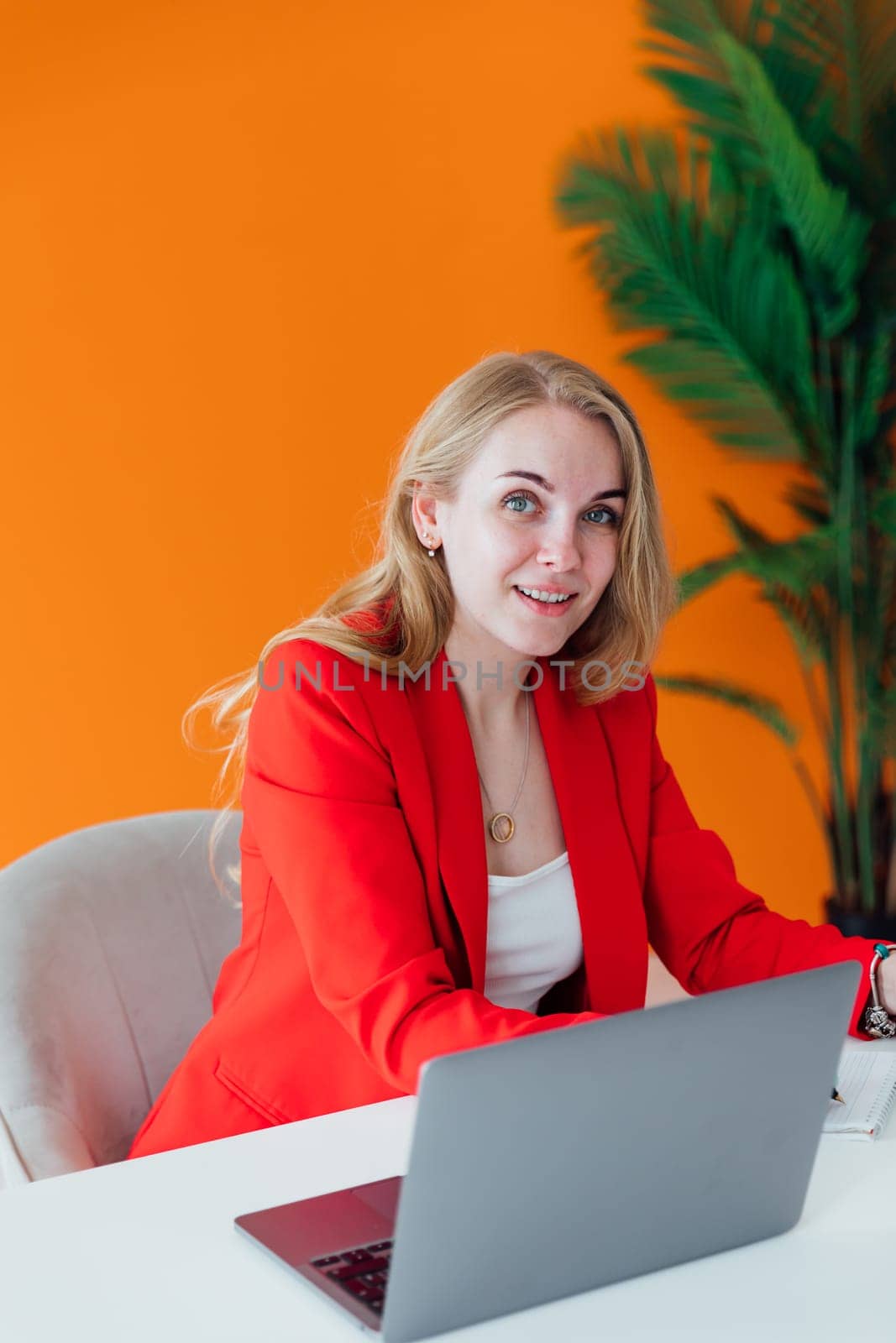 Attractive cheerful woman in red shirt working on laptop at modern office