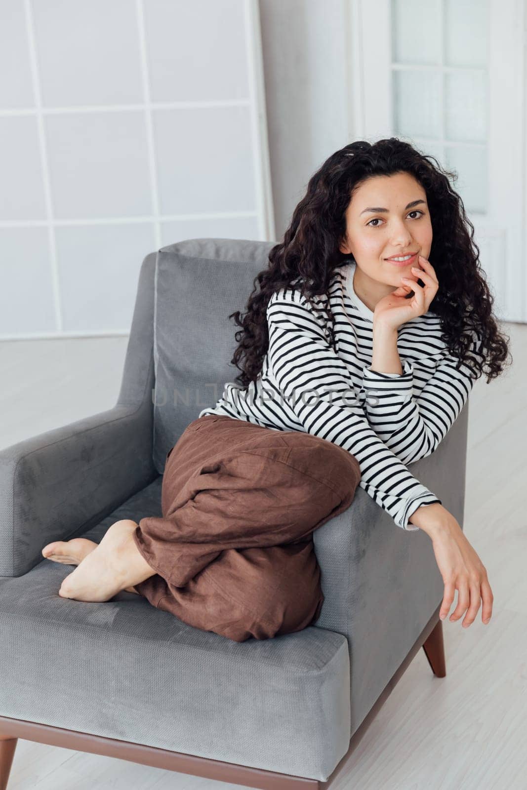 Beautiful brunette woman sitting on grey armchair by Simakov