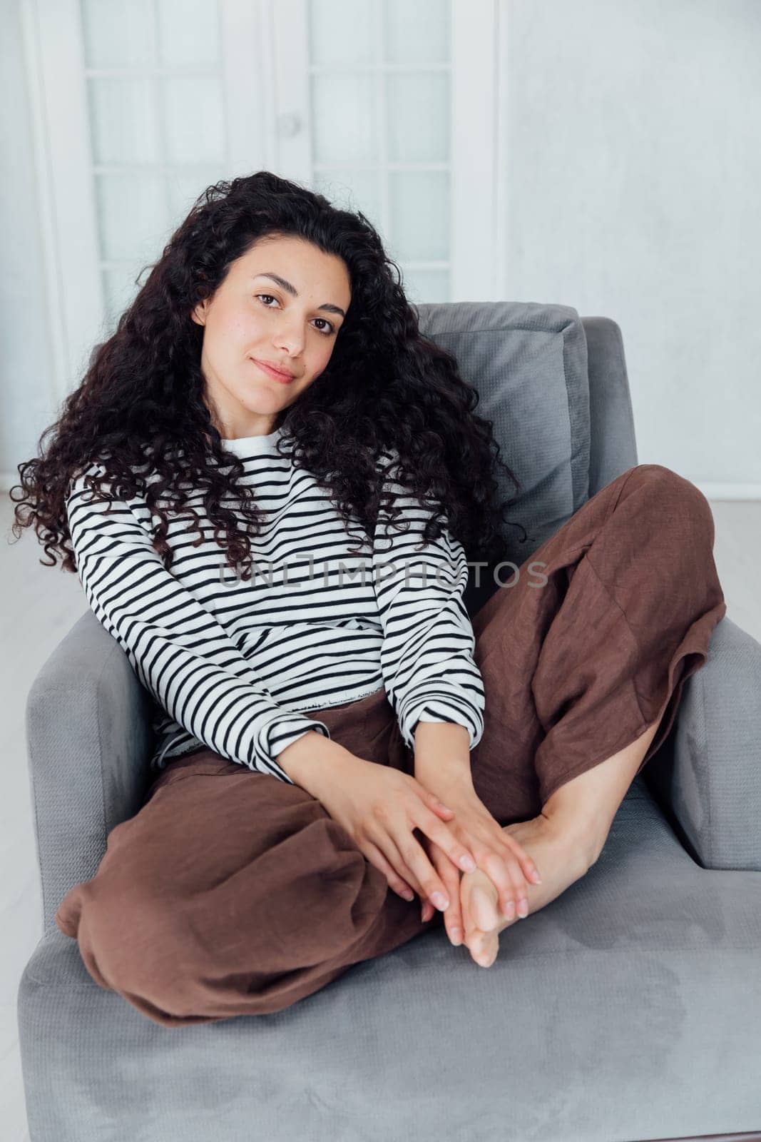 Beautiful brunette woman sitting on grey armchair by Simakov