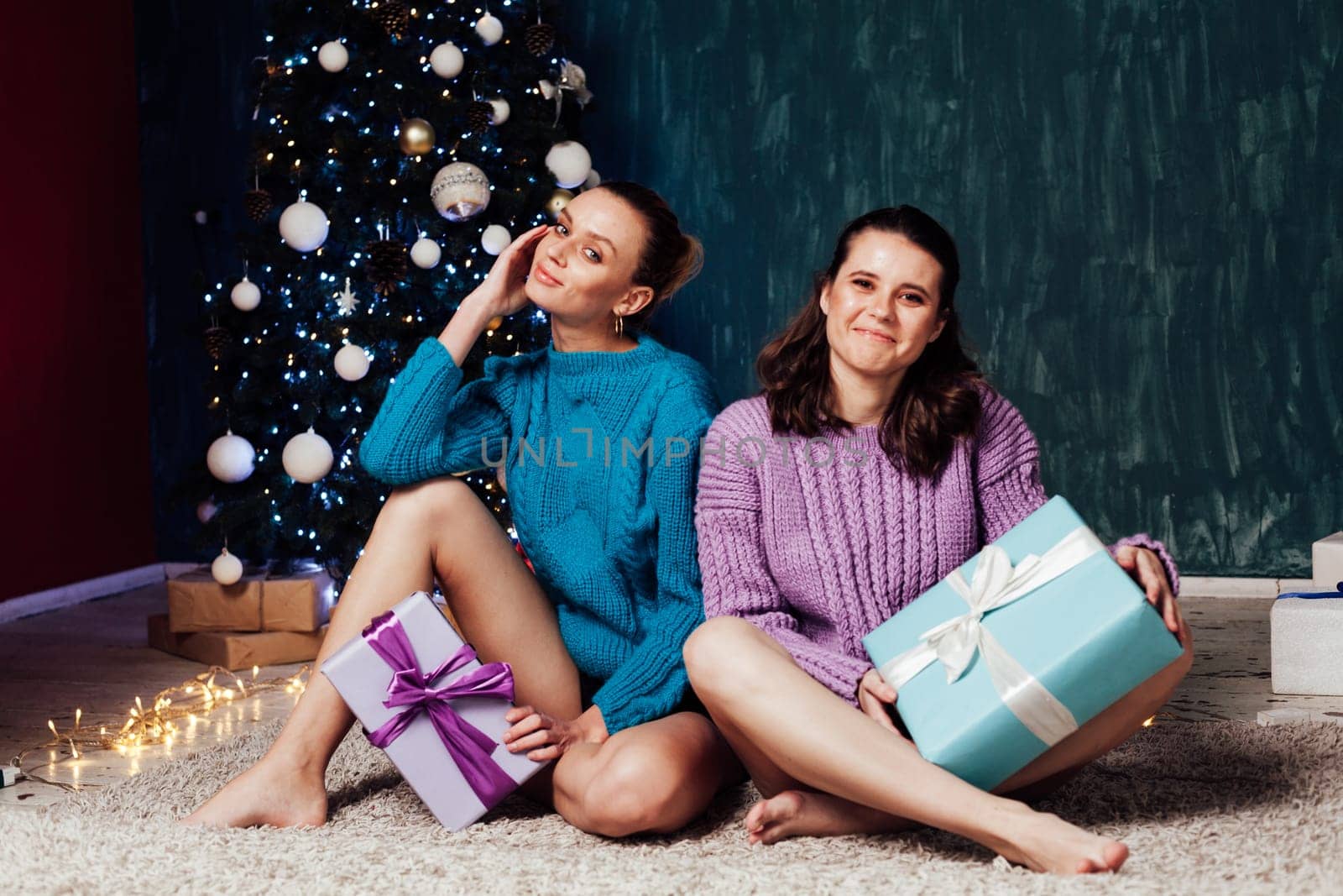 Two women friends sitting at the Christmas tree with gifts Holiday New Year