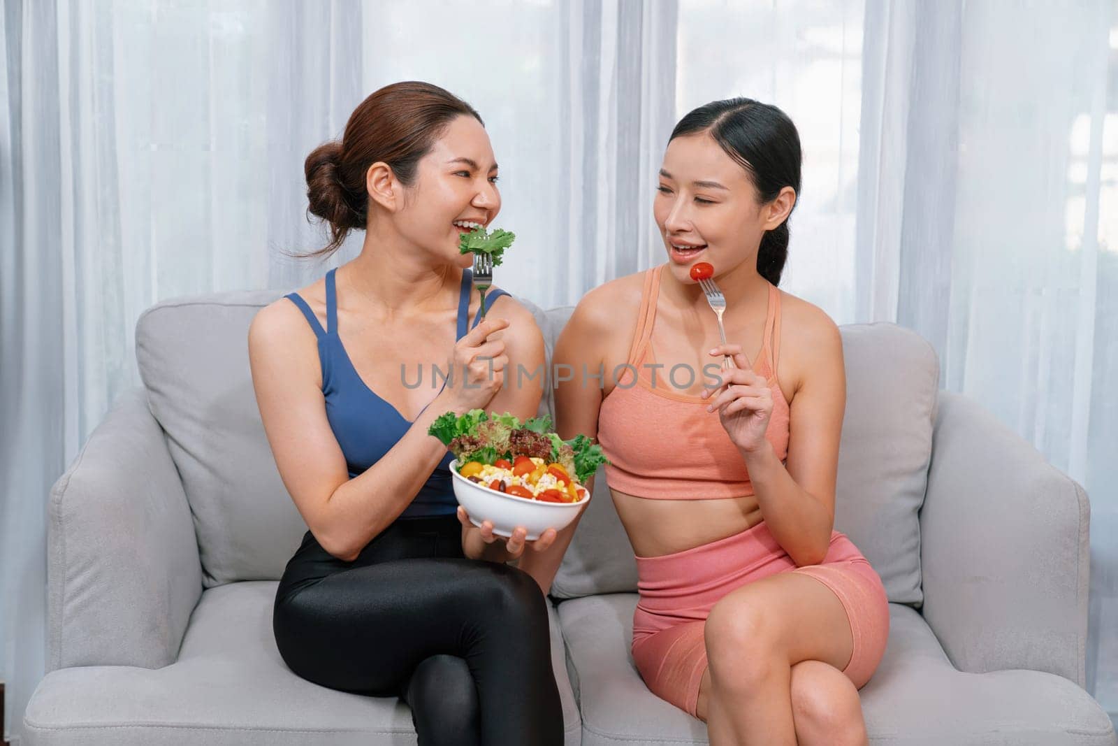 Young sporty Asian women in sportswear holding salad bowl together fill with vibrant of fruit and vegetable. Natural youthful and fit body lifestyle with balance nutrition and home exercise. Vigorous