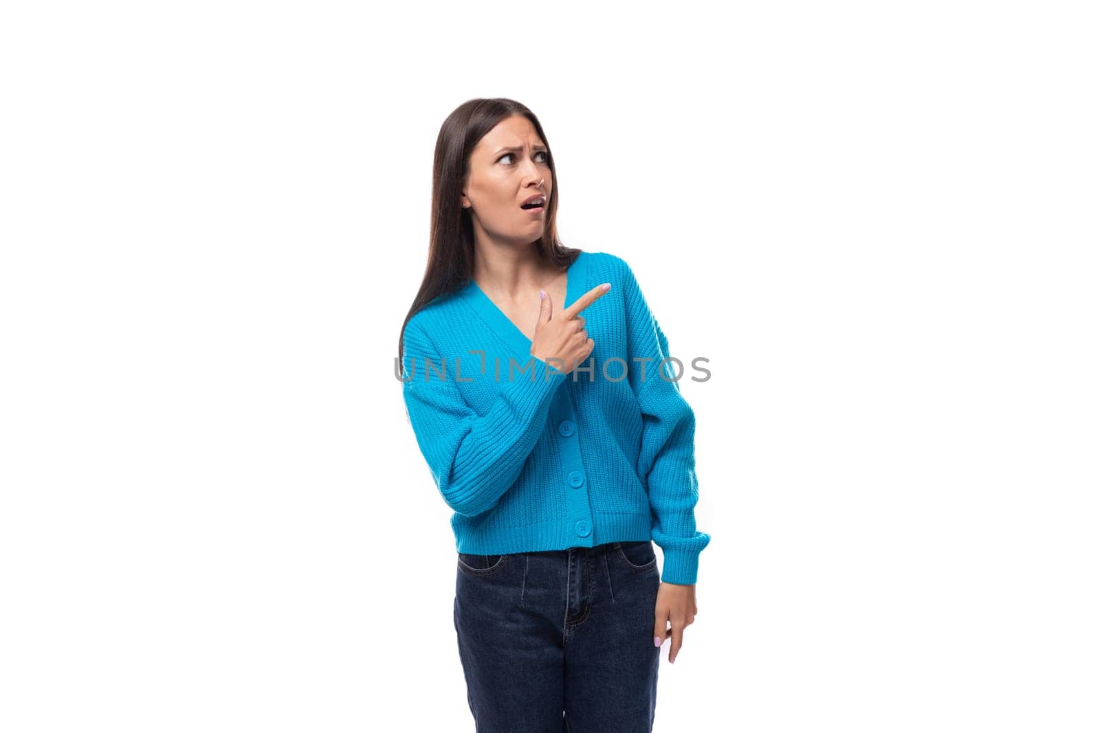 young pleasantly surprised pretty european brunette woman dressed in a blue button-down sweater rejoices on a white background with copy space by TRMK