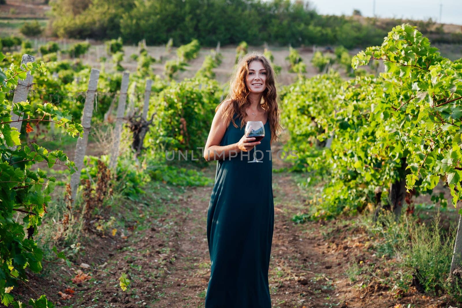 Beautiful woman with a glass of wine in a vineyard by Simakov