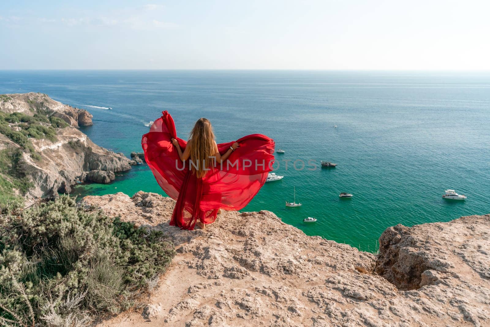 Woman sea red dress yachts. A beautiful woman in a red dress poses on a cliff overlooking the sea on a sunny day. Boats and yachts dot the background. by Matiunina