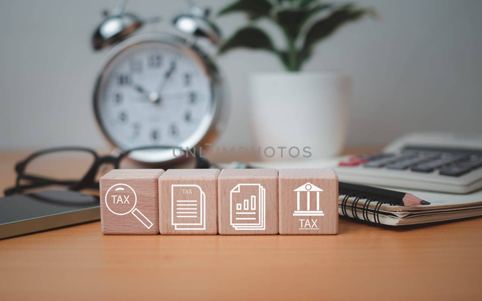 Wooden block printed tax symbols icons placed on a wooden tabletop with office supplies, financial research, reports, tax return calculations.