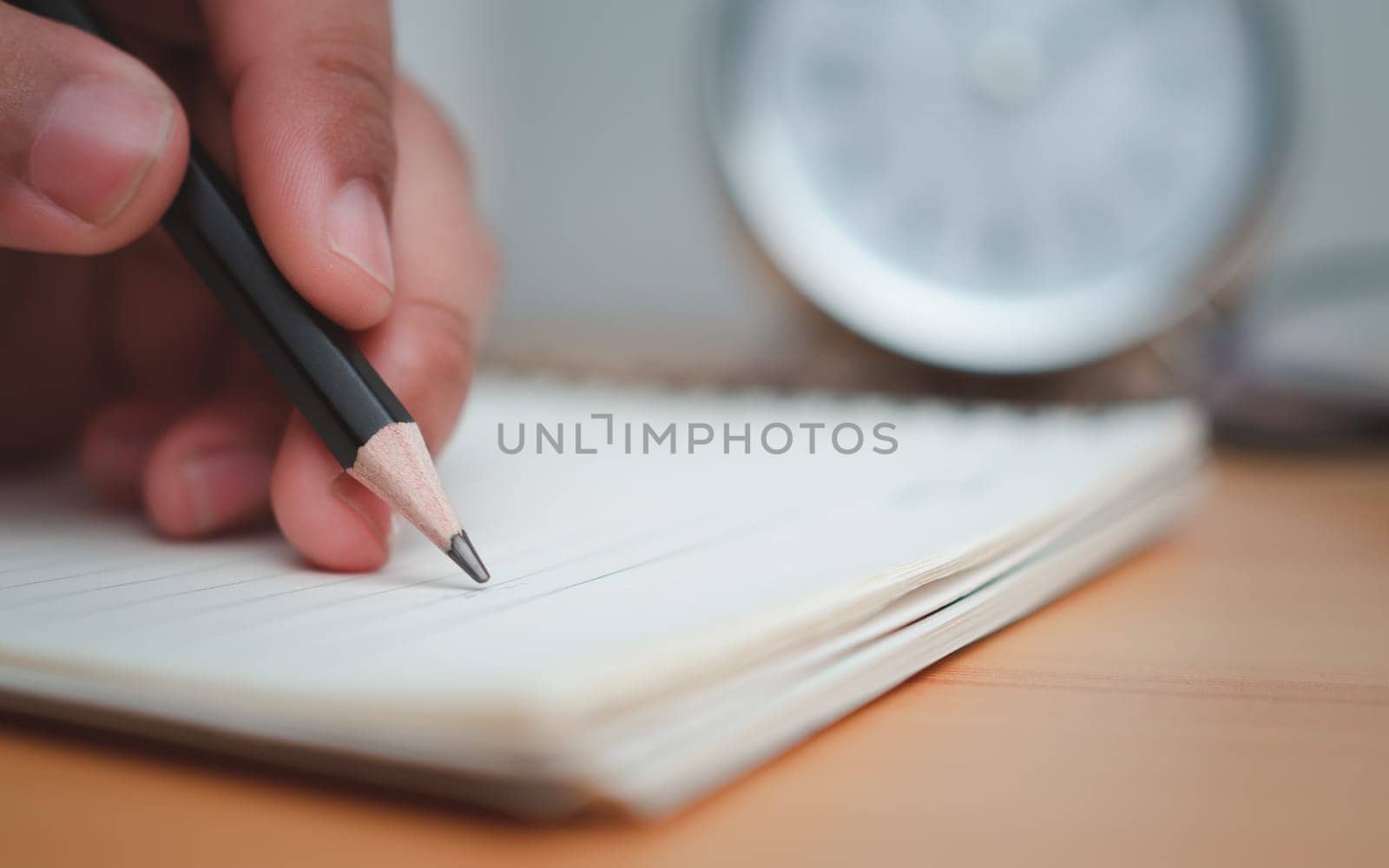 Human hands writing notes with pencil on paper on wooden table surface.