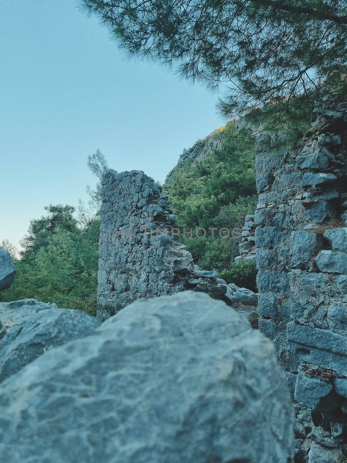 vertical photo of the ruins of ancient walls against the backdrop of green forest mountains and blue sky. soft focus