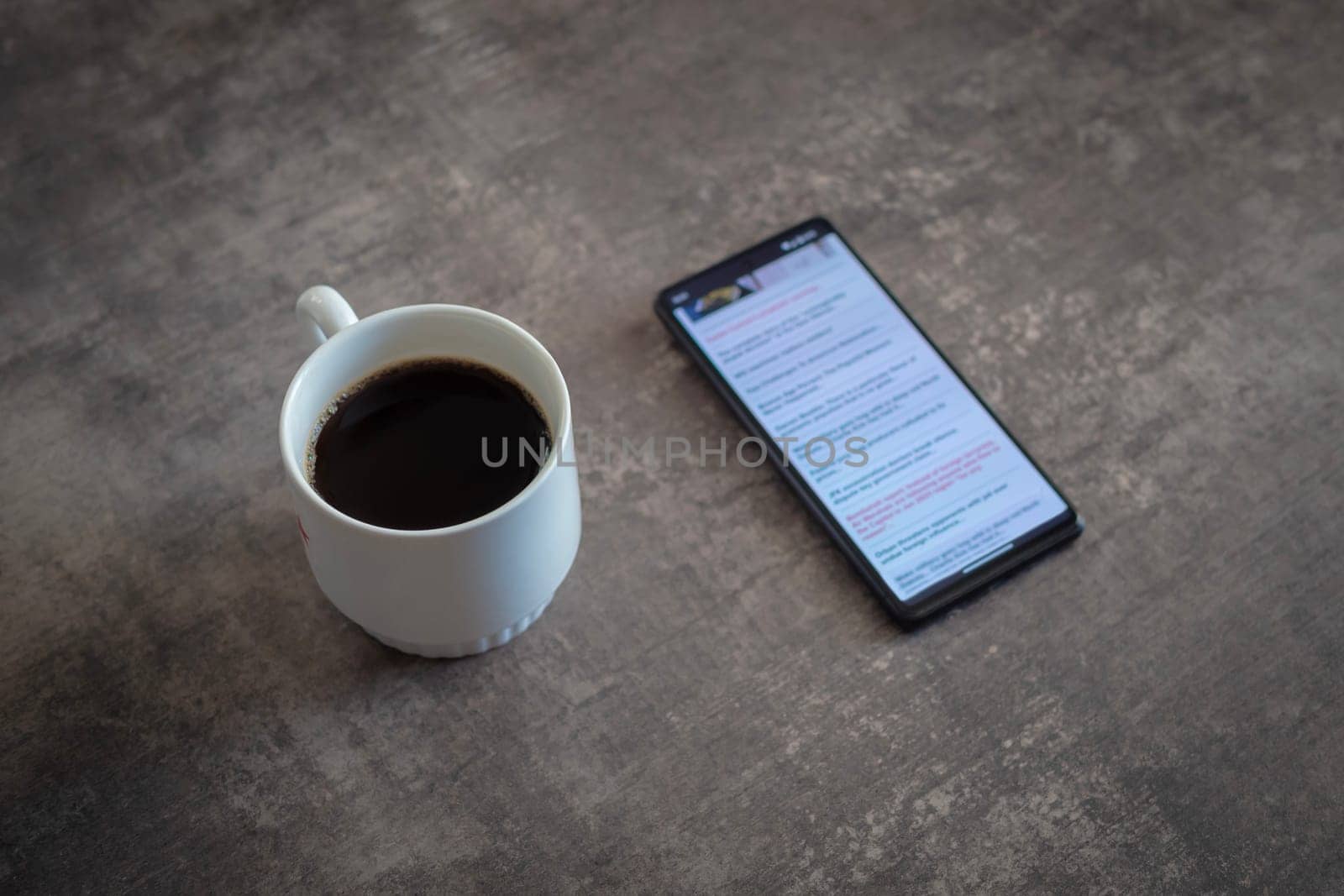 cup of coffee and smartphone with news site on screen on wooden table