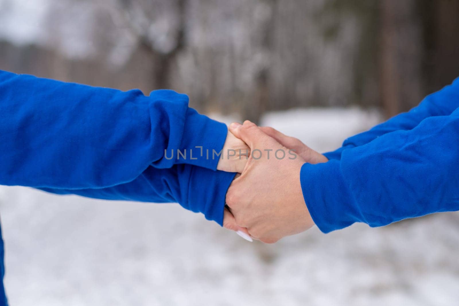 Outdoor happy couple in love posing in cold winter weather. A man and a woman in blue hoodies. Emotional young couple having fun while walking by winter forest, loving man hugging his laughing woman