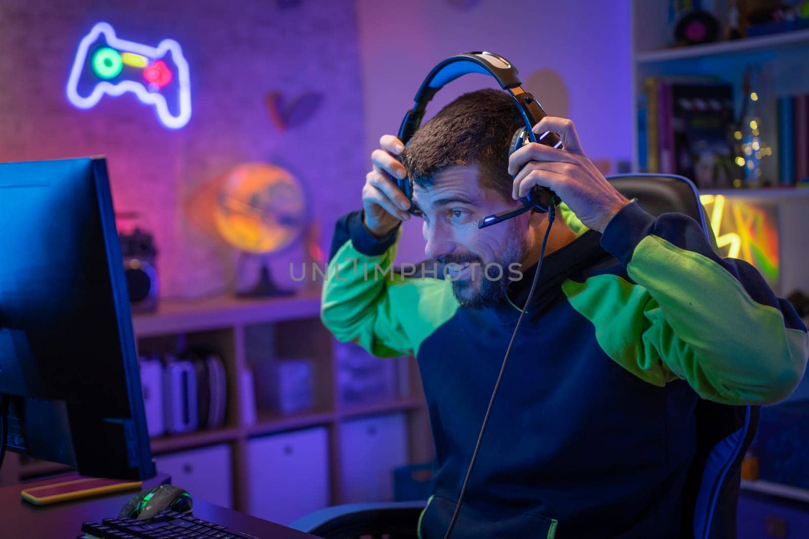 Gamer playing excited online video game with headphones streaming on computer in a neon light room. by PaulCarr