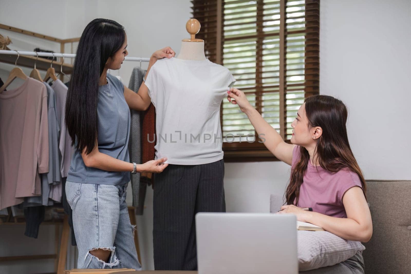 Asian couple chatting livestream to sell clothes and showing clothes to customers while selling at home. by wichayada