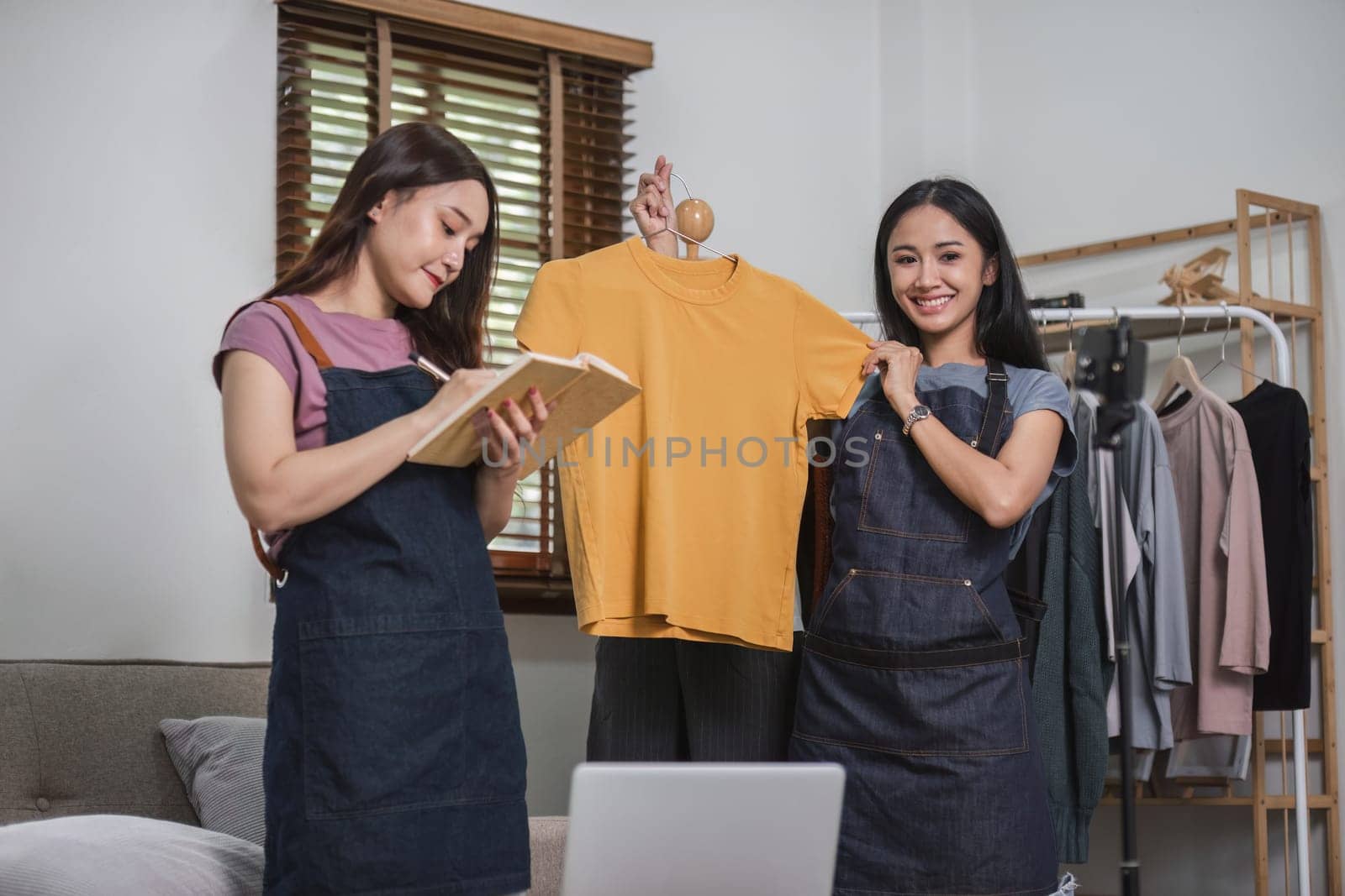 Asian couple chatting livestream to sell clothes and showing clothes to customers while selling at home..