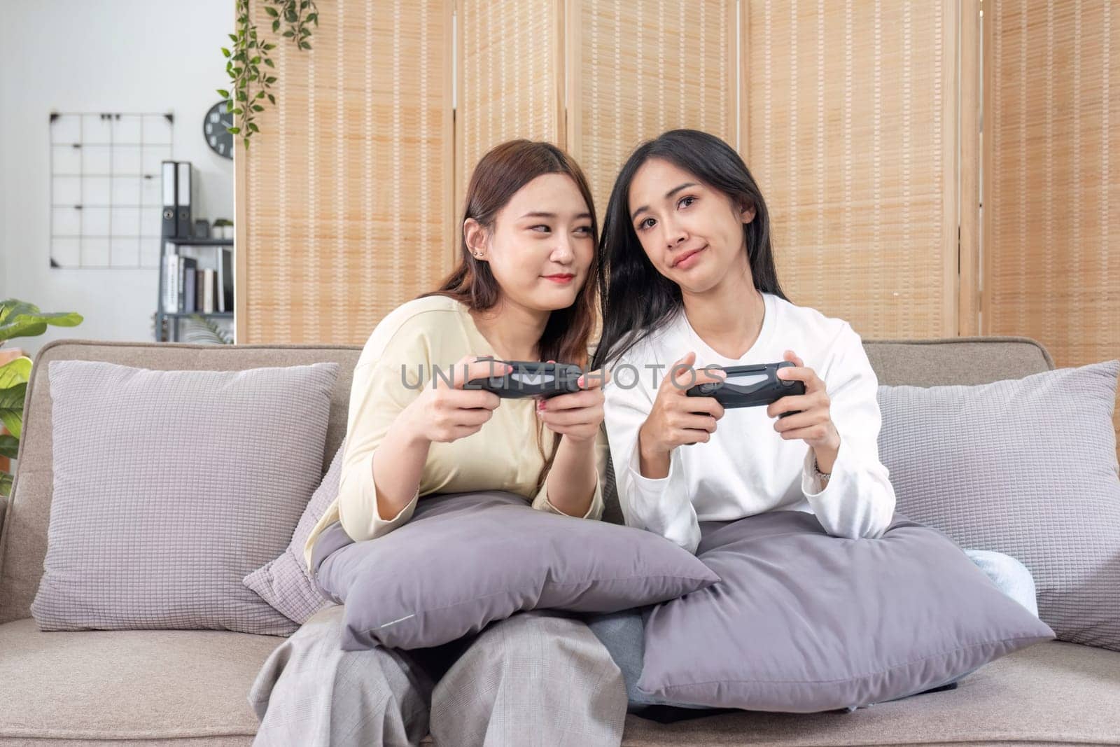 Young Asian couple playing video games at home in the living room having fun. by wichayada