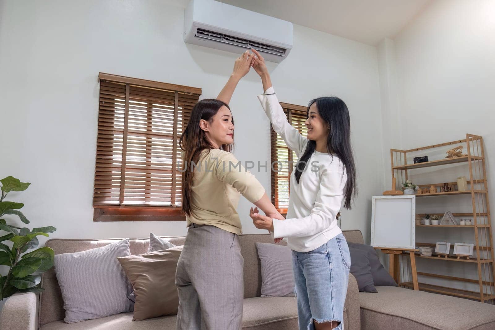 Beautiful young Asian lesbian couple dancing in the living room at home, fun mood. LGBT concept of sex and happy living together.