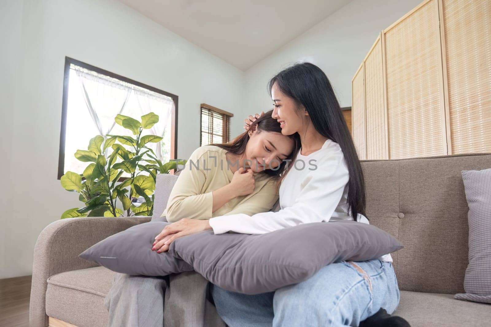 a young couple sitting together on the sofa in the living room warmly. by wichayada