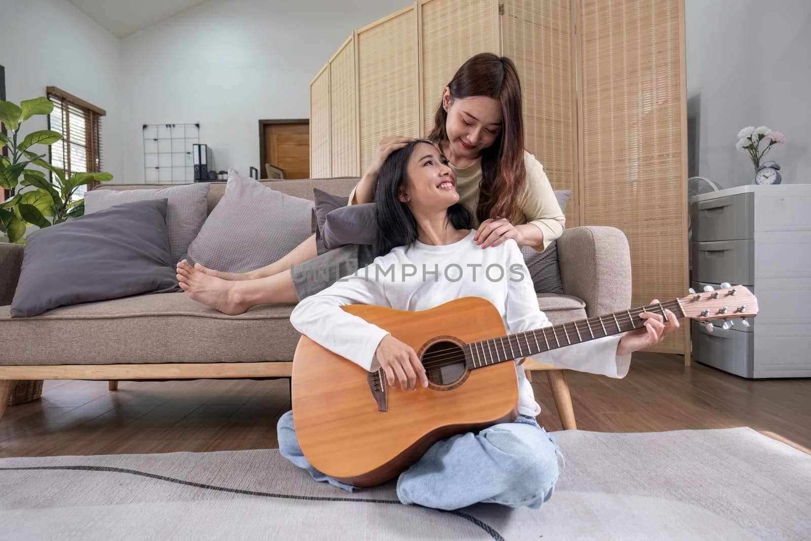 LGBT. Two young women play guitar and sing in the living room too together for a happy time..