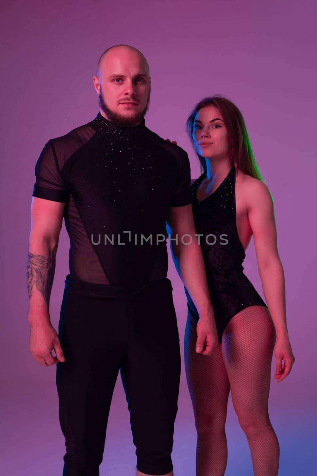 Charming woman and an athletic male in a dark sport suits are looking at the camera and posing in a studio against a colorful background. Gymnasts performance.