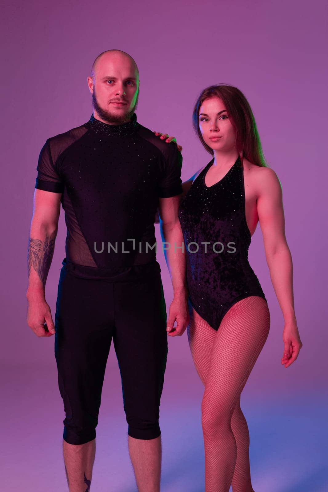 Beautiful girl and an athletic man in a dark sport suits are posing in a studio against a colorful background. Gymnasts performance.