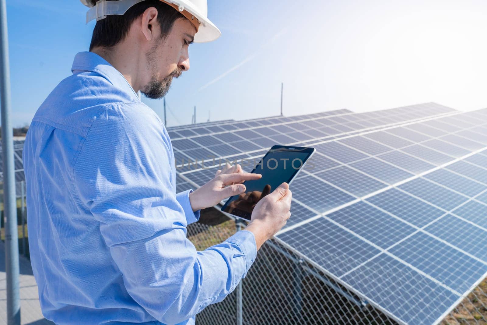 Engineer working with a tablet with photovoltaic solar panel system plant in the background. Green clean energy concept.